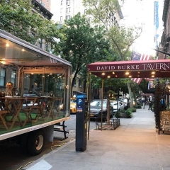 Glass Truck outside DBT on 62nd Street showing red awning of David Burke Tavern and clear view to tables inside glass walled cube truck